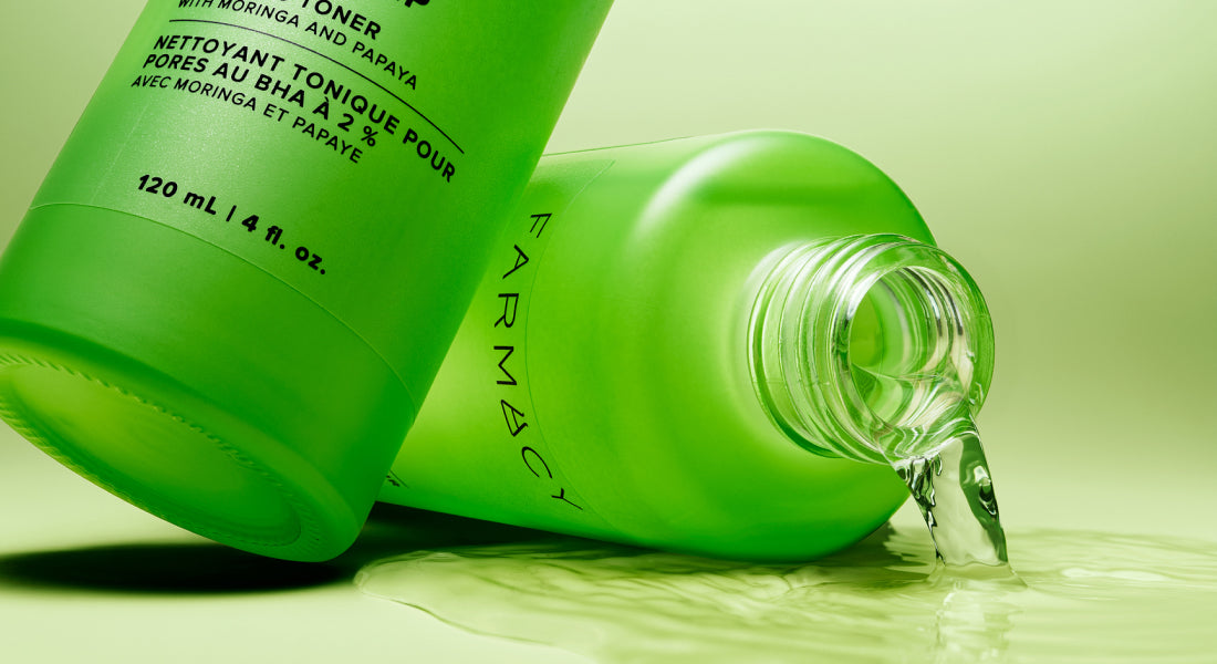 Green skincare bottle with liquid spilling out on a light green background
