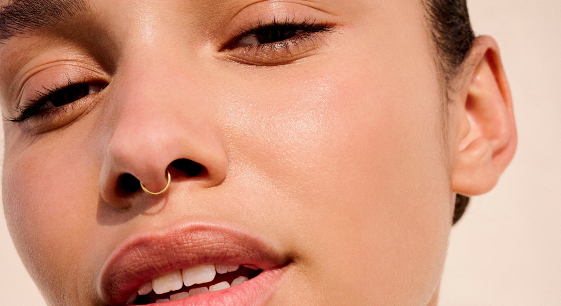 Close-up of a person's face with a gold nose ring on a beige background