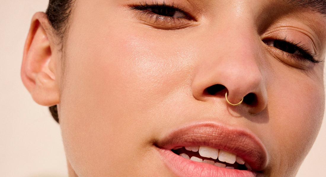 Close-up of a person wearing a gold nose ring with a neutral background