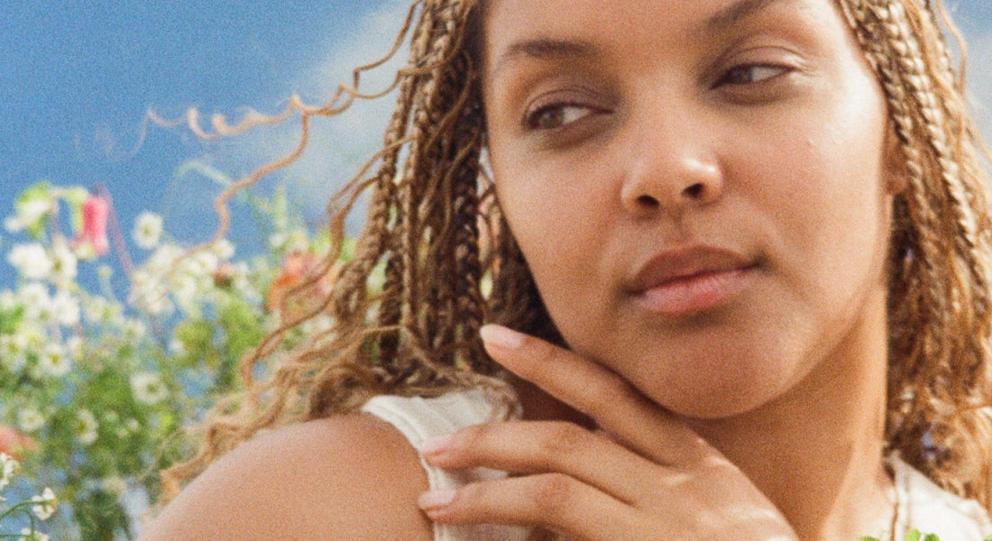 Woman with braided hair in a natural setting with flowers and blue sky